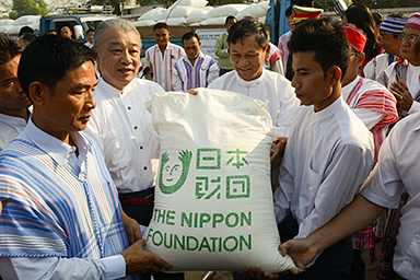 Photo of The Nippon Foundation Chairman Yohei Sasakawa delivering rice to grateful representatives of an ethnic group in Myanmar