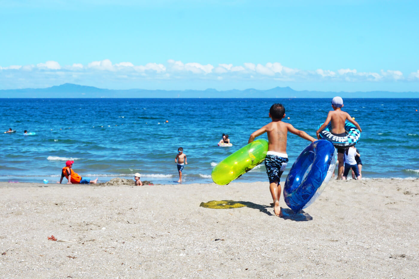 写真：浮き輪など抱え、海で遊ぶ子どもたち