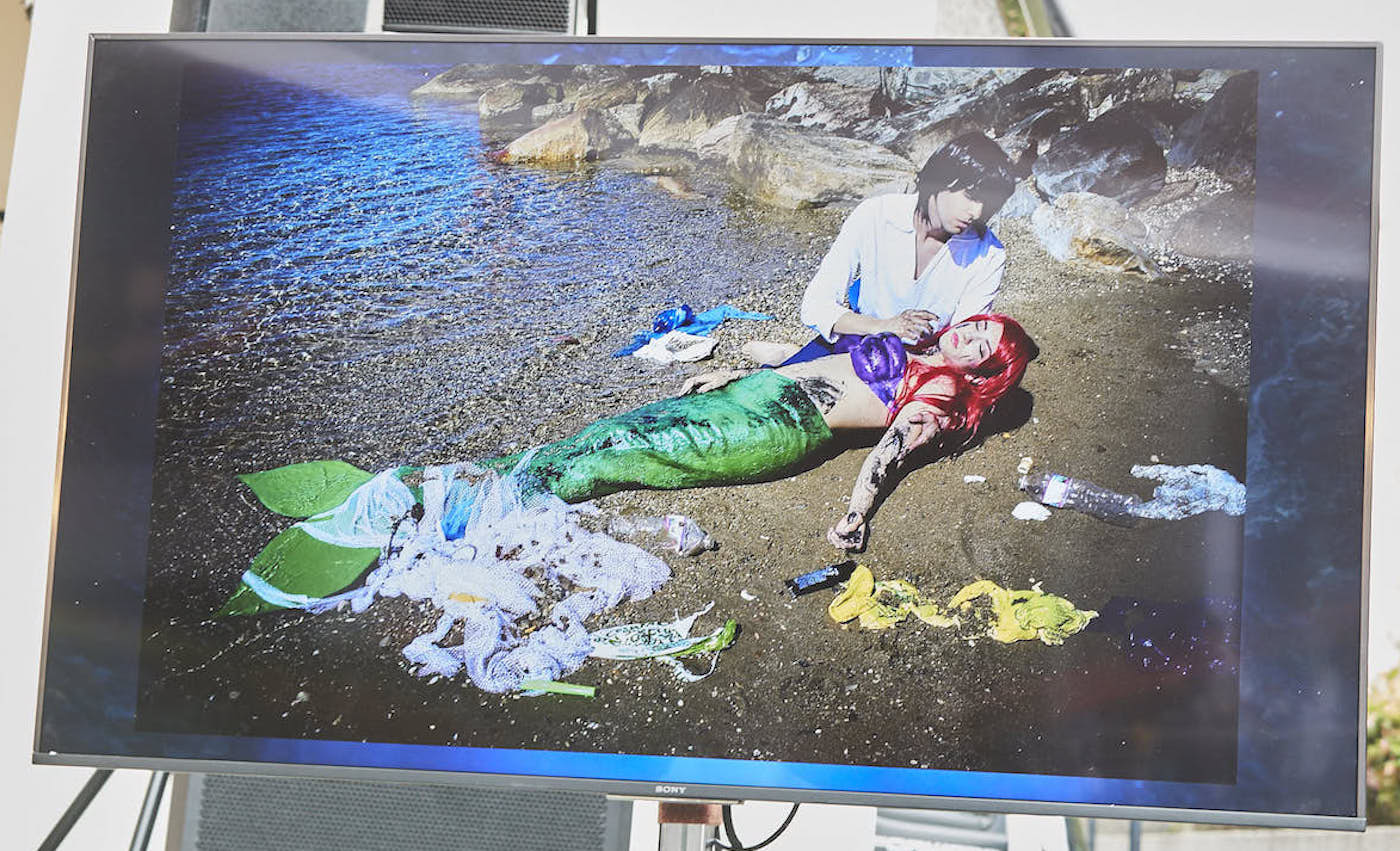 写真:海洋ごみに囲まれ瀕死の状態を表現する、リトルマーメイドのキャラクターに扮したデイジーさんとイムリエルさん。