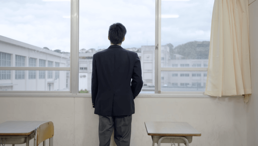 写真:窓の外を教室の中から見つめる生徒の後ろ姿