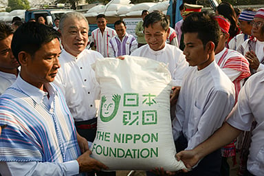 Photo of The Nippon Foundation Chairman Yohei Sasakawa delivering rice to grateful representatives of an ethnic group in Myanmar