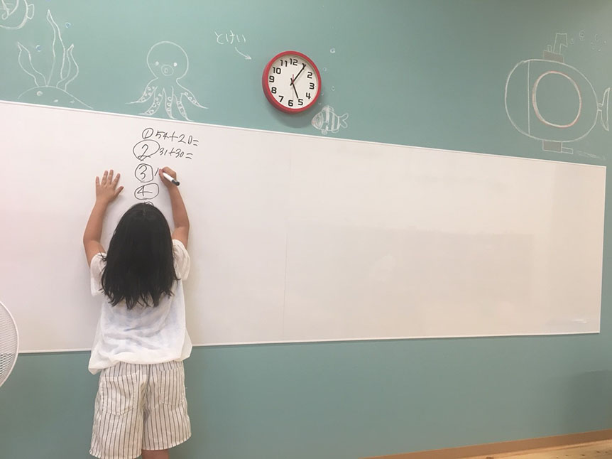 写真:壁のホワイトボードに足し算を書く女の子