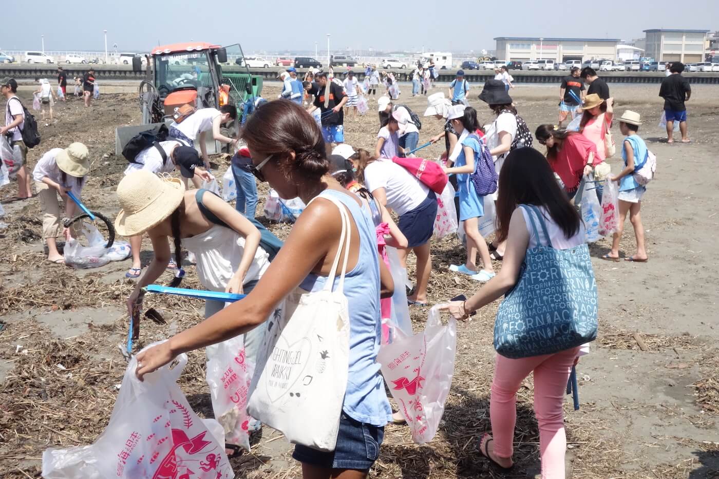 写真：ごみ袋とトングを使って海辺のごみ拾いをする大人や子どもたち