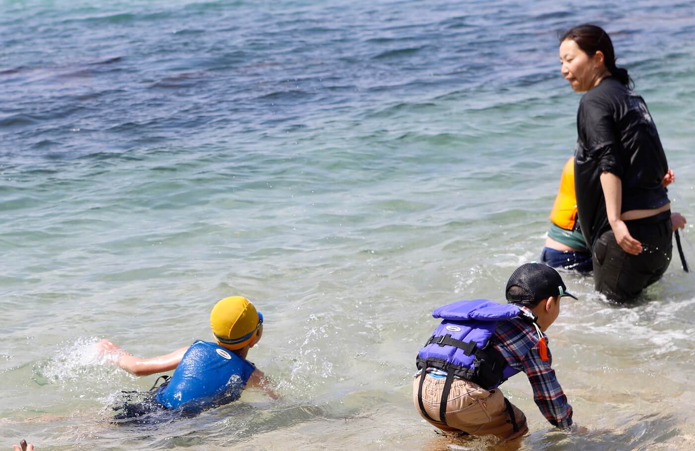 写真：海で遊ぶ子どもたちと女性