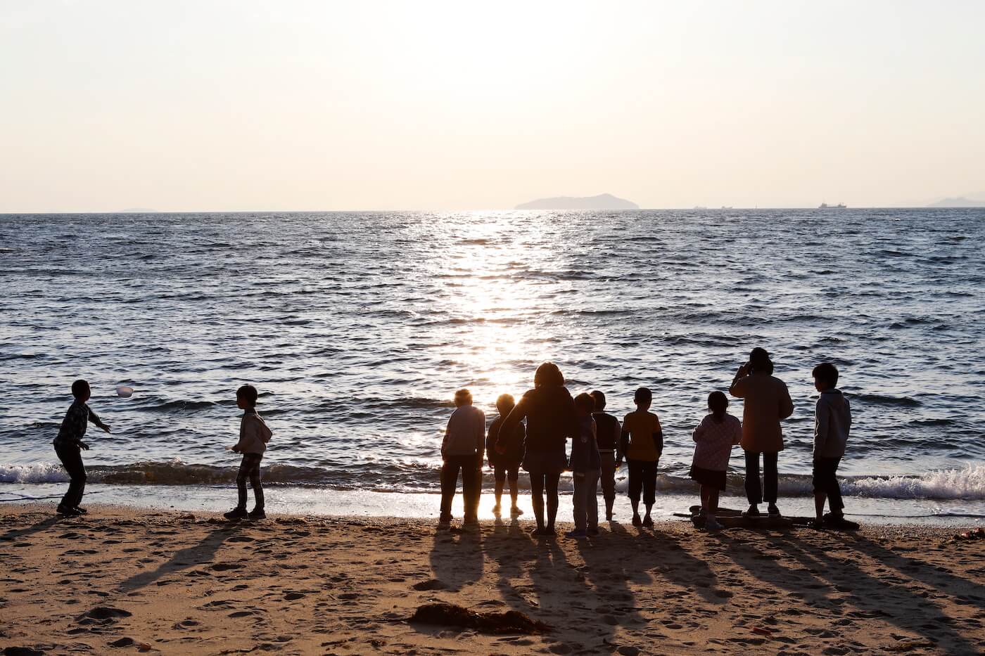 写真；夕暮れの海岸に集う子どもたち