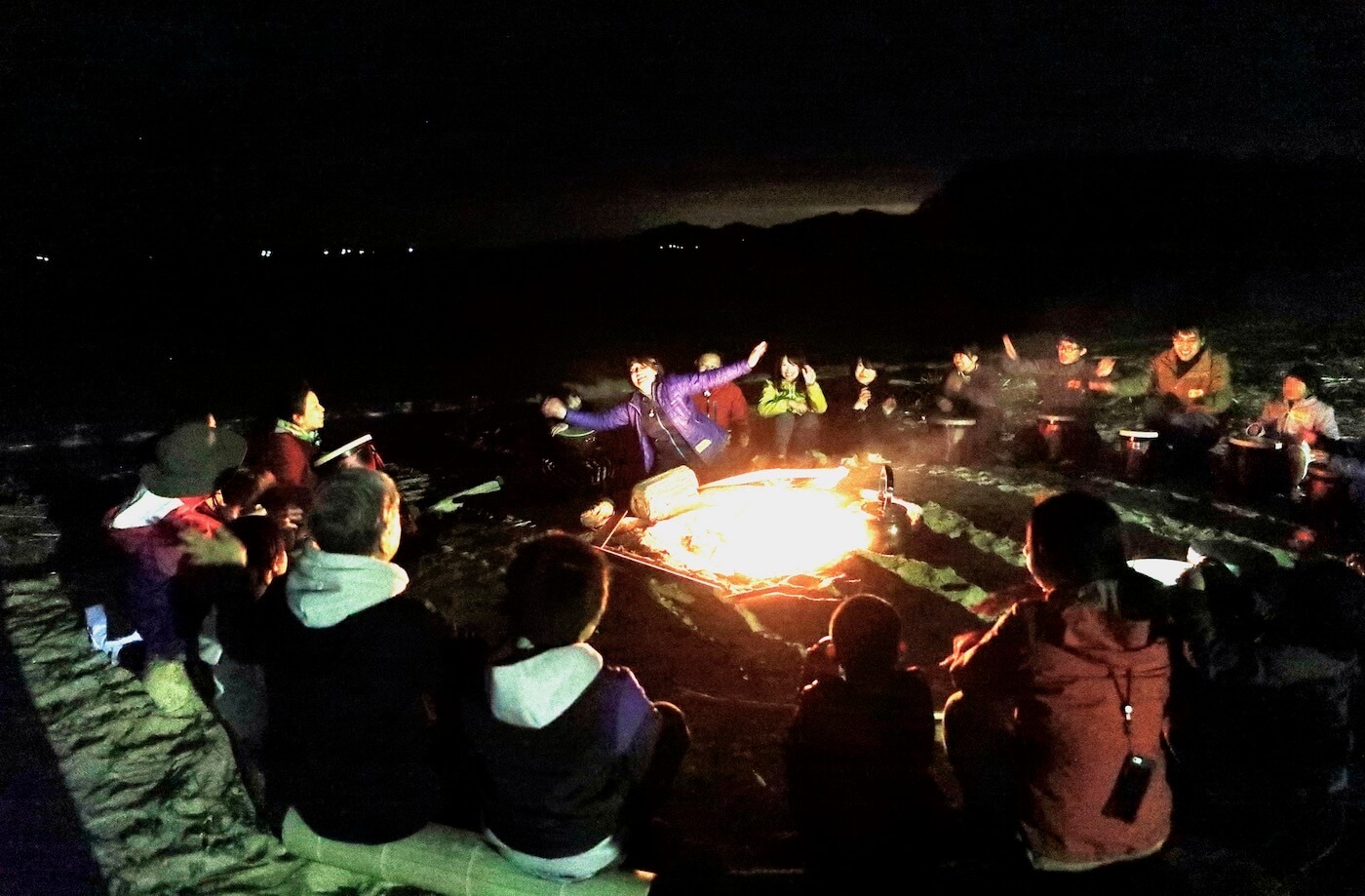 写真：夜の海岸で大きな焚き火を囲む大勢の大人や子ども