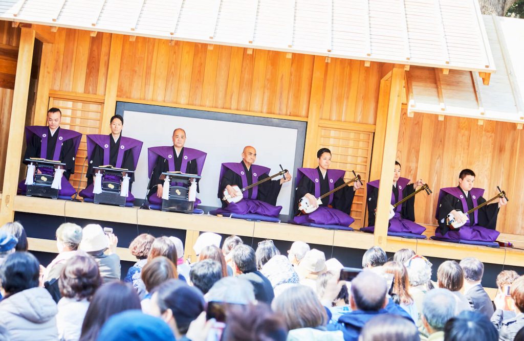 写真：舞台の上で演奏する三味線奏者たちと待機する太夫たち。それを鑑賞する大勢の観客