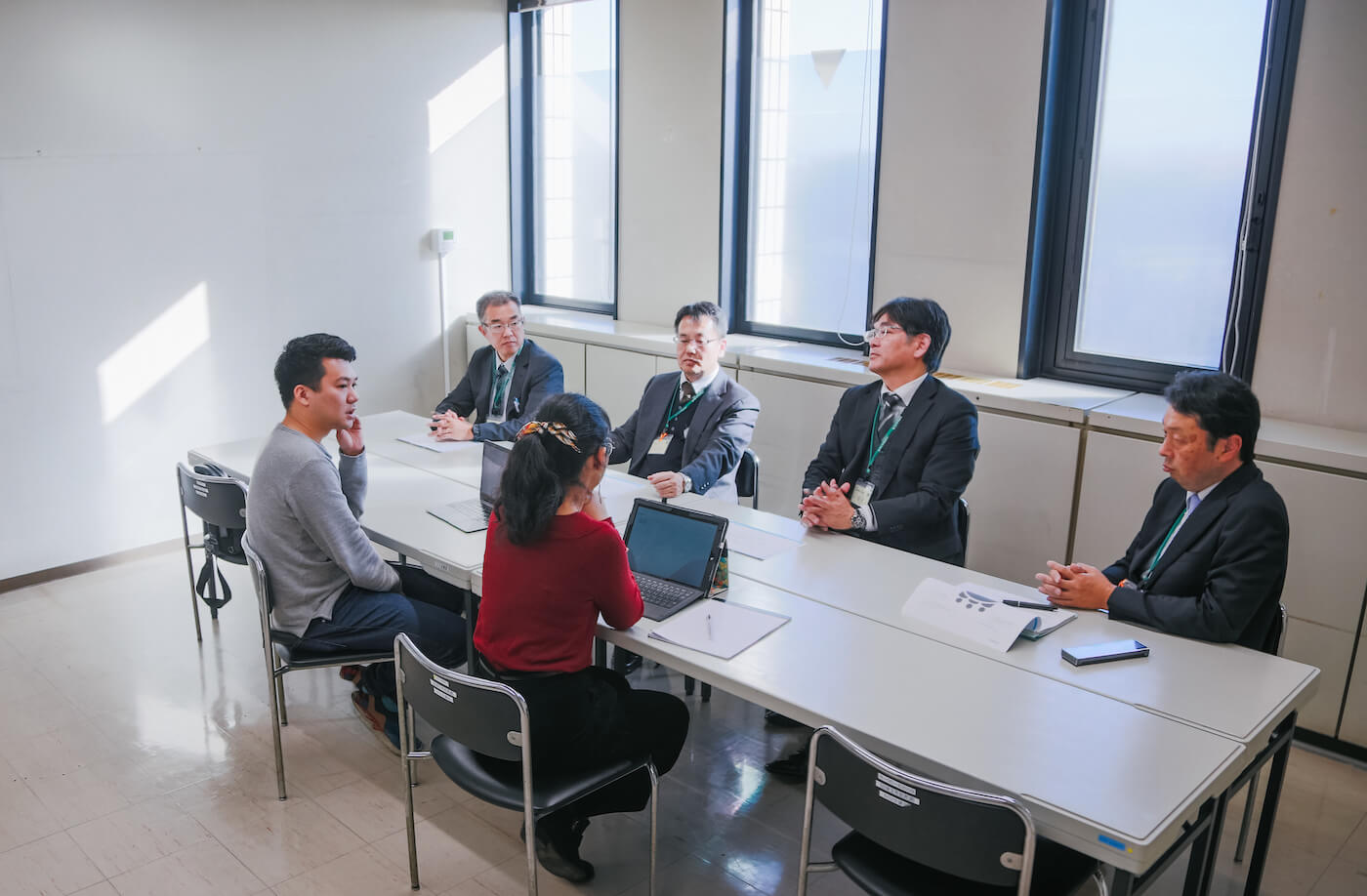 写真：学校の一室で複数の先生と話をする浅谷さんとアローズのスタッフ