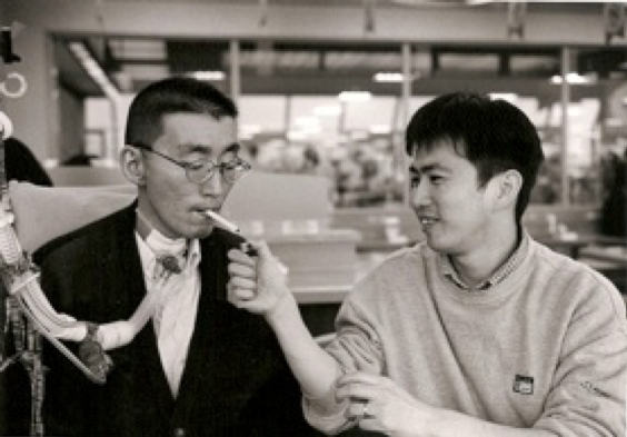 写真:鹿野さんが口に咥えるタバコに、笑みを浮かべながら火を付けるボランティアの男性