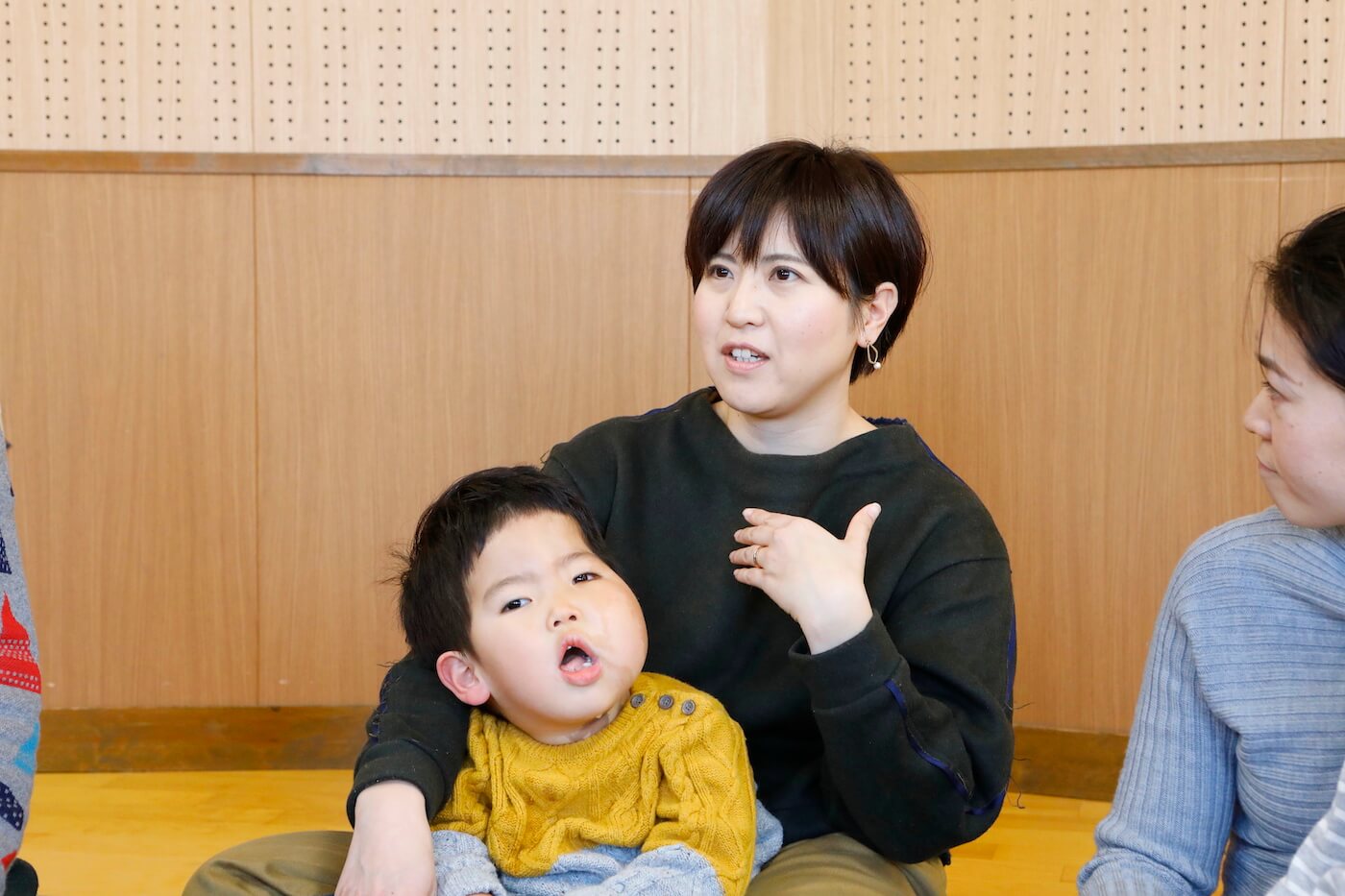写真:インタビューに答える嵯峨さんの奥さんと、膝の上に抱かれる嵯峨さんのお子さん