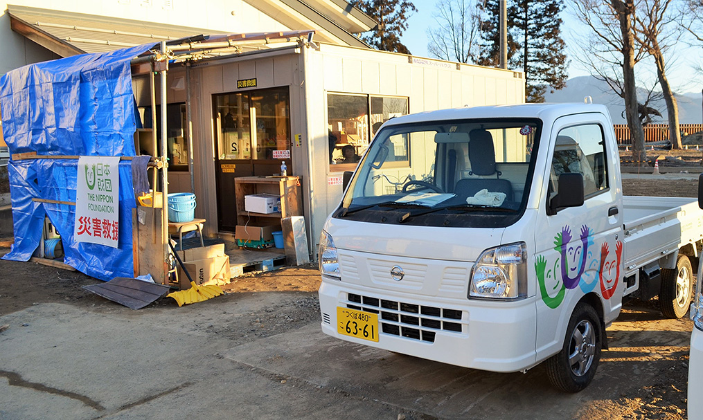 写真：長沼体育館前にある支援活動の拠点のプレハブ小屋と、日本財団が被災地に寄贈した軽トラック