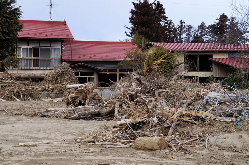 写真：家屋の近くに放置された流木と土砂。流木が2階の高さまで積み上がっていました