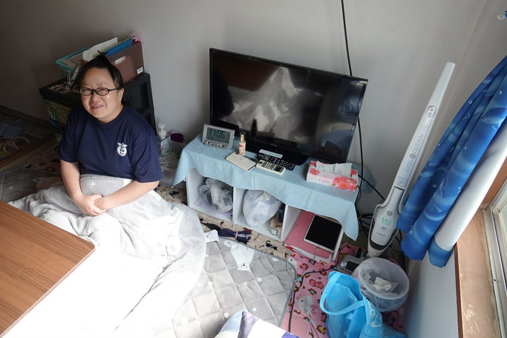 写真：下宿の居室で真新しい家電製品に囲まれて笑顔を見せる女性 