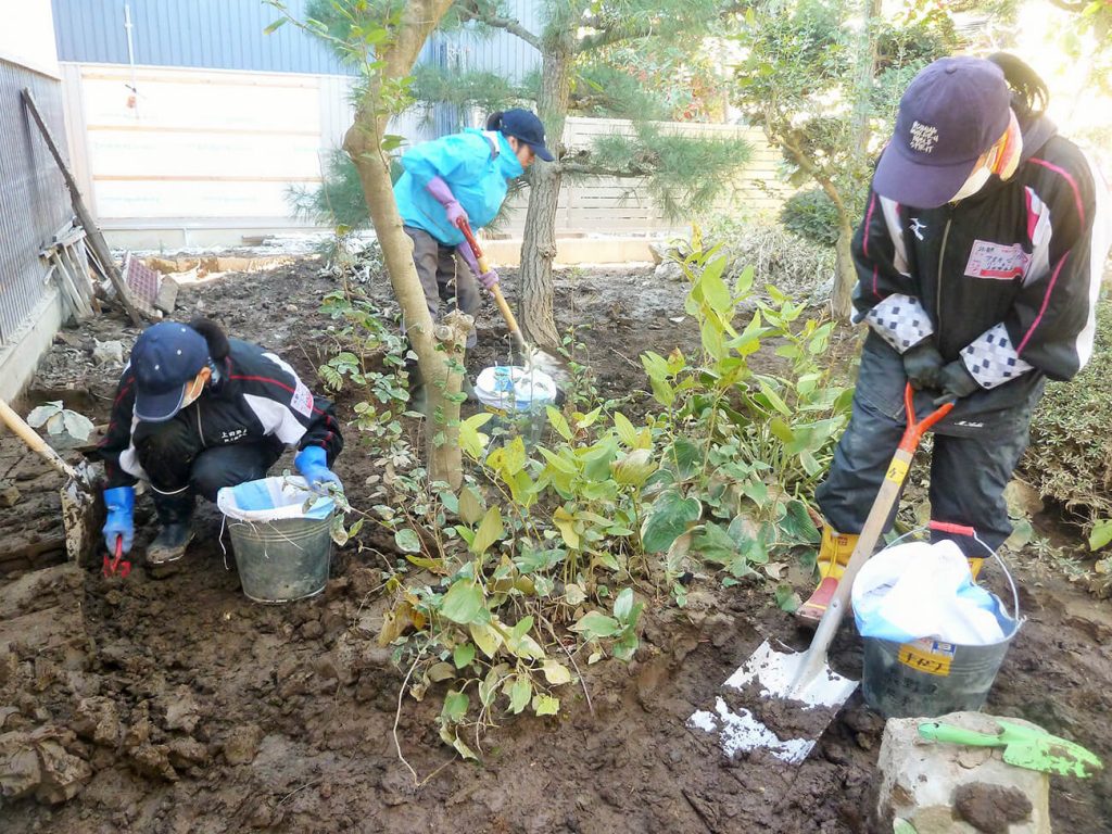 写真：被災して泥がたまった住宅の庭で、スコップを手に泥を掘って外に出す作業をする高校生の様子（2019年11月9日、横沢祥子さん提供）