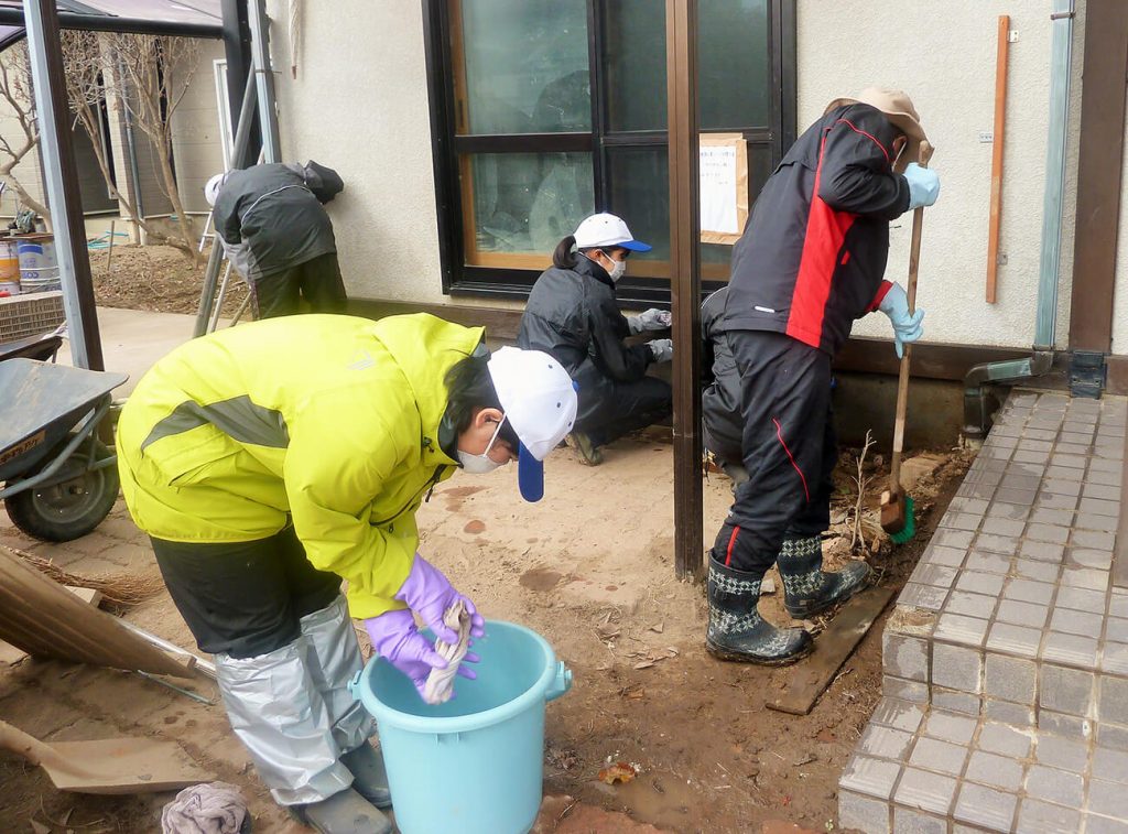 写真：被災した住宅の庭で、バケツなどを使って掃除をする高校生の様子（12月14日、横沢祥子さん提供）