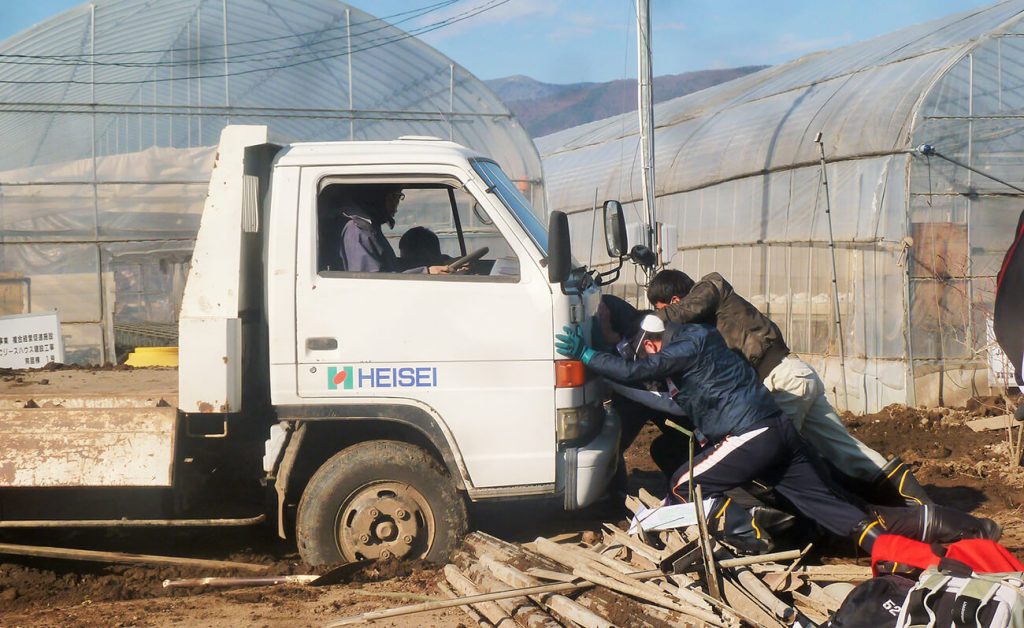写真：被災地の畑で立ち往生した白いトラックを助けるため、車の前方から複数で力強く押す高校生の様子（12月14日、横沢祥子さん提供）