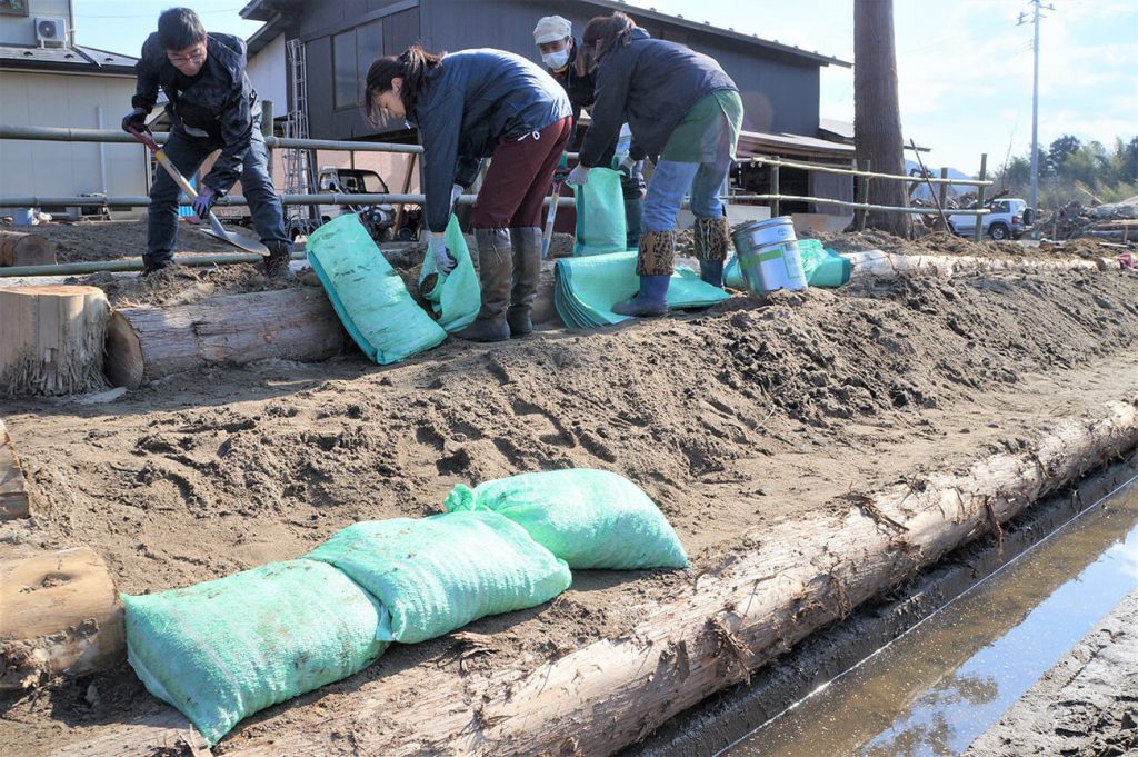 写真：緑色の土のう袋に、ショベルを使って土砂を詰めるスマイルシードスタッフたち