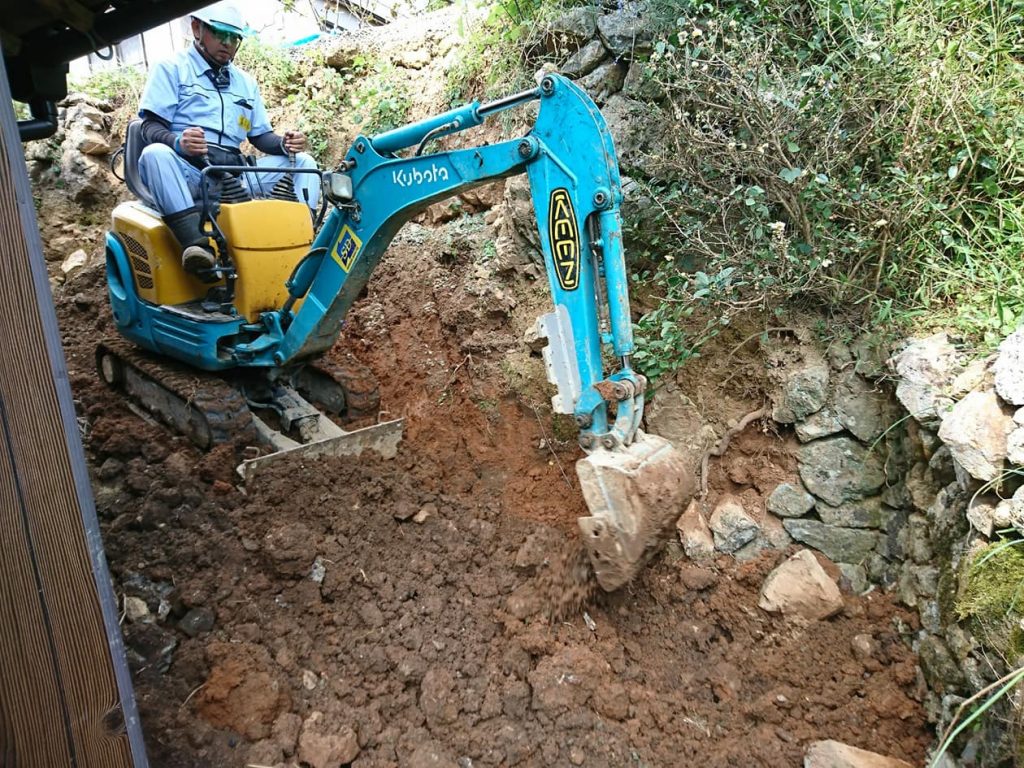 写真：西日本豪雨の被災地・愛媛県西予市で、土砂でできた斜面の上で重機を操作する萬代さん（2018年10月、萬代さん提供）