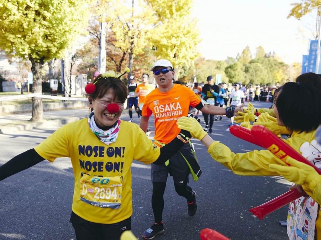 写真：大阪マラソンにて笑顔で走る日本クリニクラウン協会のメンバーと、それを応援する観客