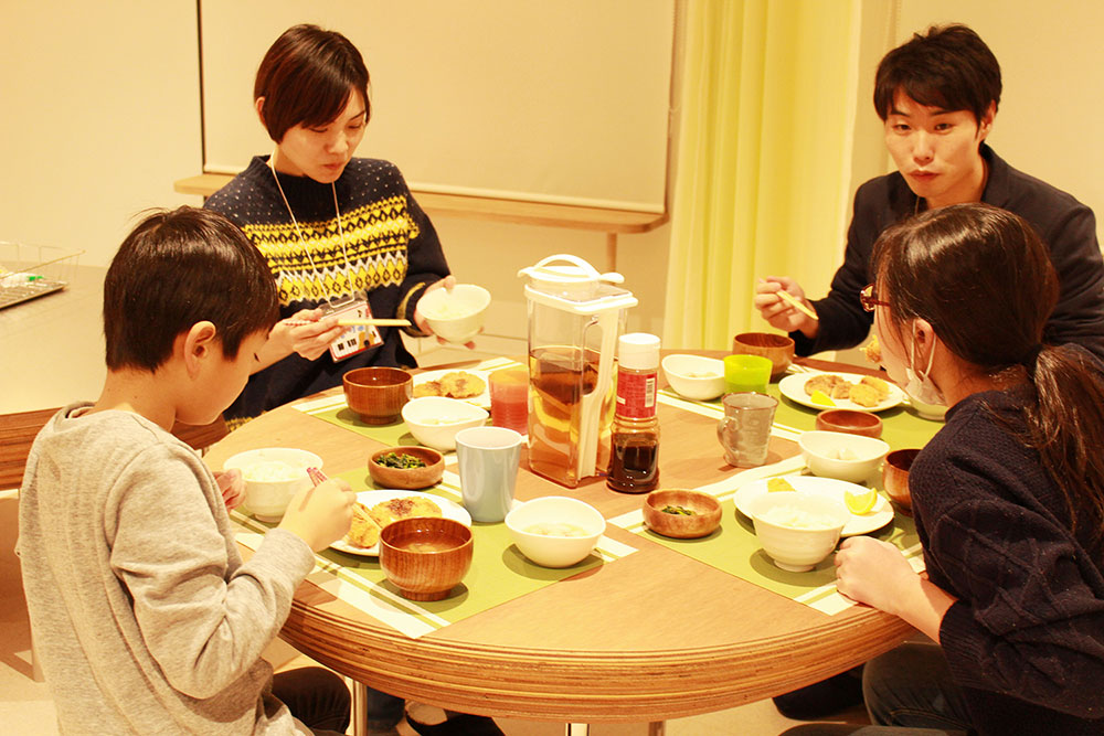 写真:大人2名、子供2名で食卓を囲み食事をする様子