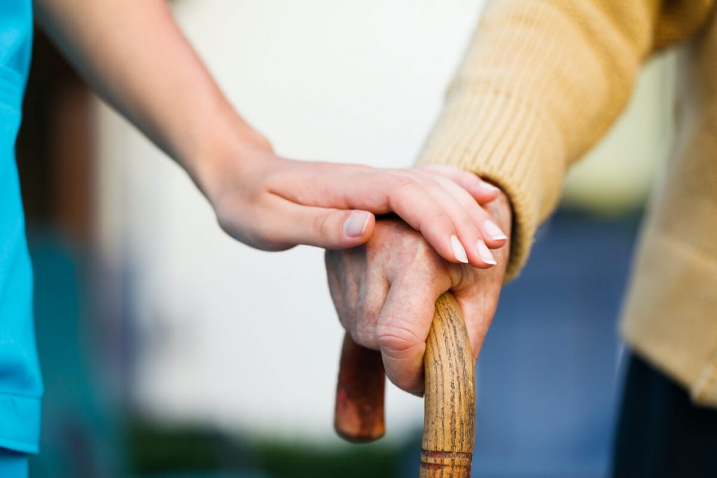 写真：杖をつく高齢者の手を取る介護士の手