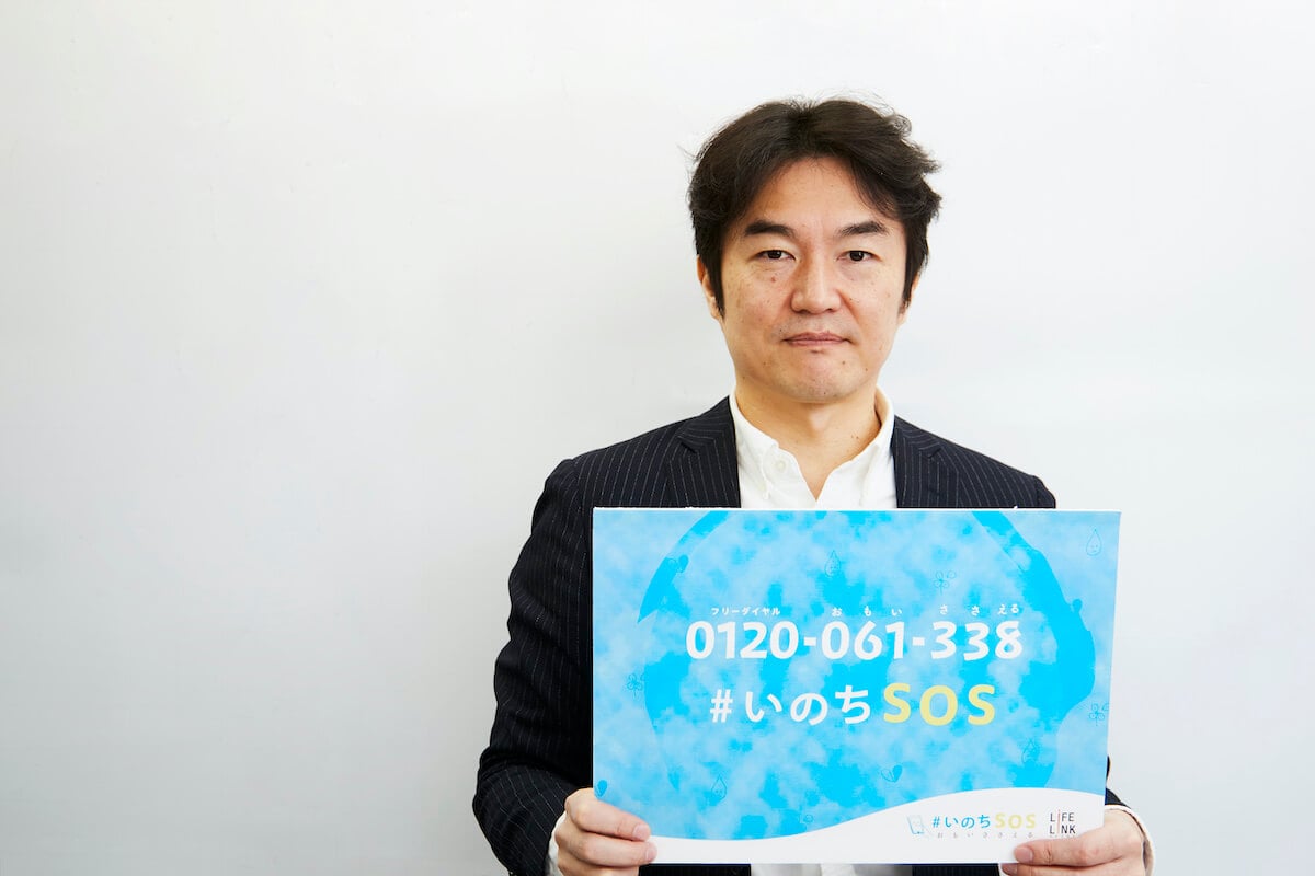 写真：電話相談窓口「＃いのちSOS」のPR用ボードを手に持つ清水さん