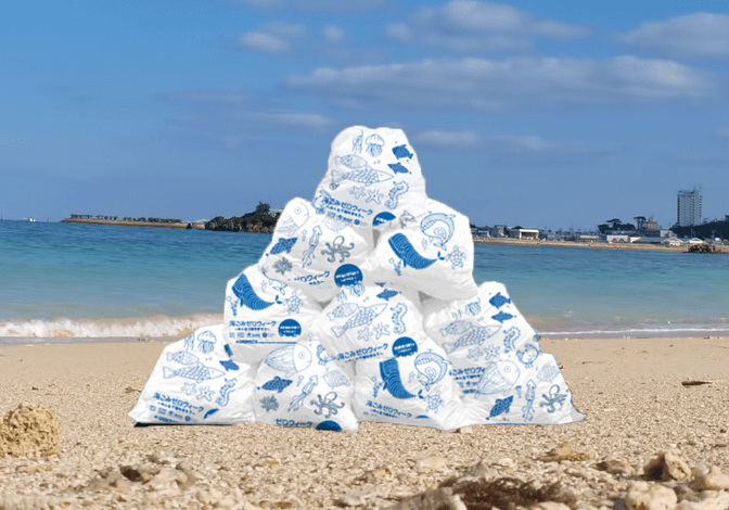 写真：オリジナルごみ袋に回収され海辺に積み上げられたゴミ。海洋ごみを減らせば多様性ある豊かな海になることを表現
