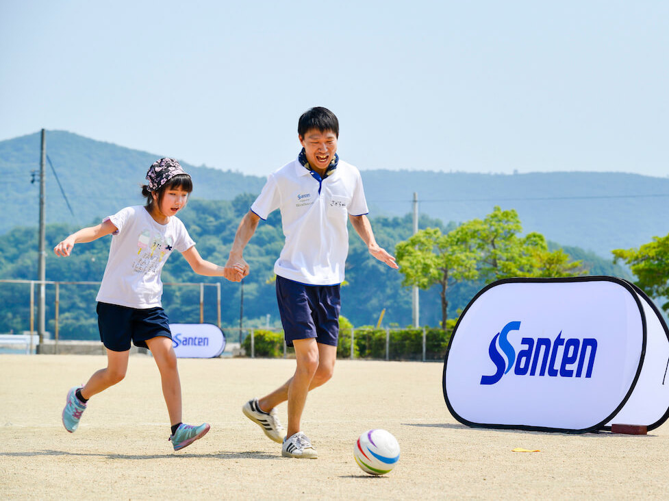 写真：ブラインドサッカーを体験する視覚障害のある子どもと、手をつなぎ指導するスタッフ