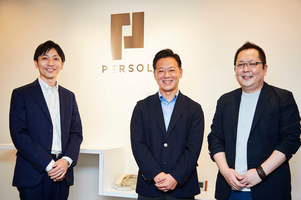 写真：PERSOLのロゴの前で笑顔を向けるパーソルチャレンジ株式会社の戸田さん、木田さん、大濱さん