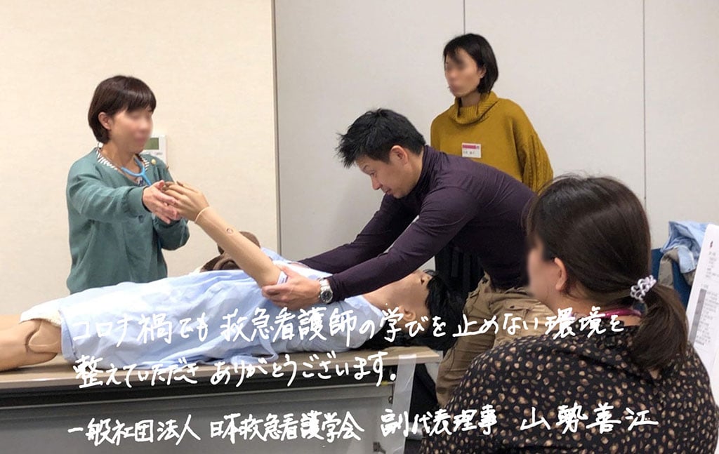 写真:セミナーの集合教育の様子。画像下側にメッセージ「コロナ禍でも救急看護師の学びを止めない環境を整えていただきありがとうございます。一般社団法人 日本救急看護学会 副代表理事 山勢善江」の文字