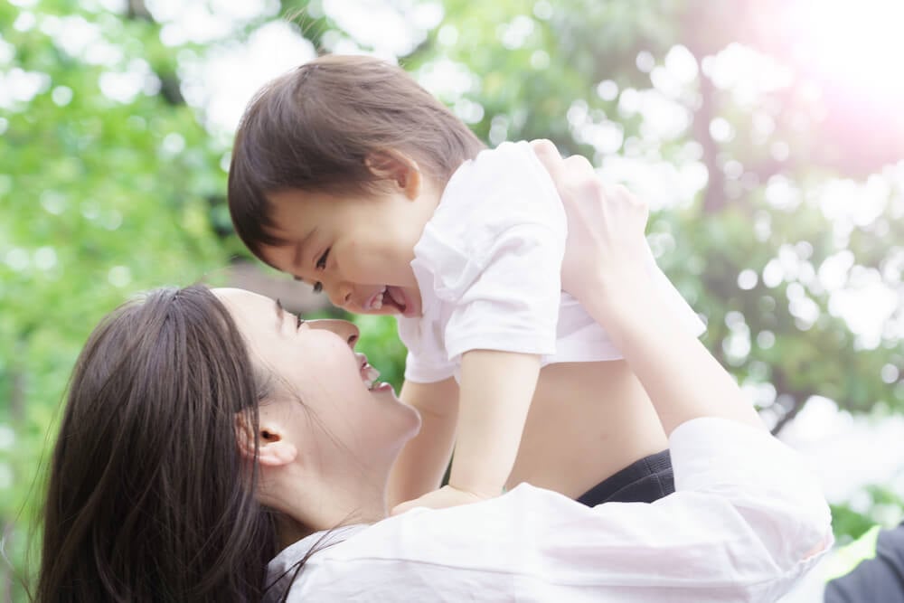 写真:喜ぶ幼子を笑顔で抱き抱える母親