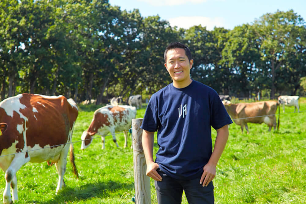 写真:牛たちのいる牧場に笑顔で立つ長沼さん