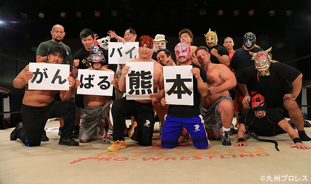 写真：リング上に集合し「がんばるバイ熊本」のプレートを胸に掲げる九州プロレスの選手たち