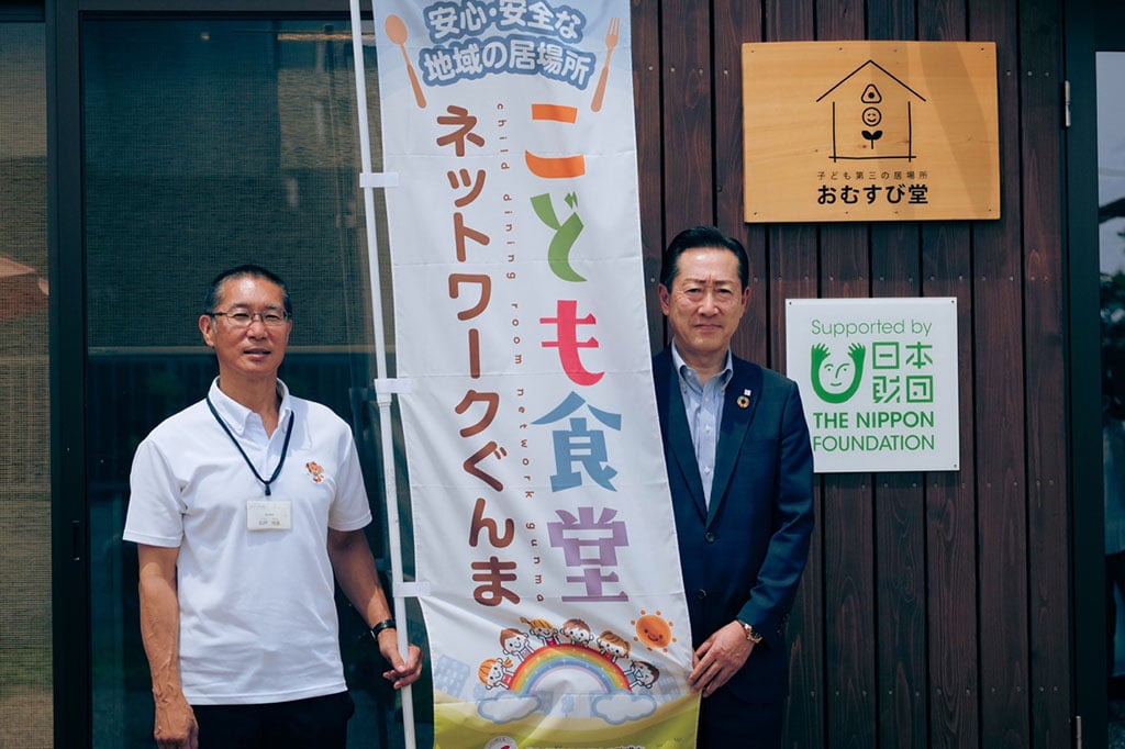 写真:群馬県みどり市の子ども第三の居場所の前に立つ、社会福祉法人チハヤ会 施設長の石戸悦史さん(左)と大栄産業株式会社 代表取締役社長の戸塚和昭さん(右)
