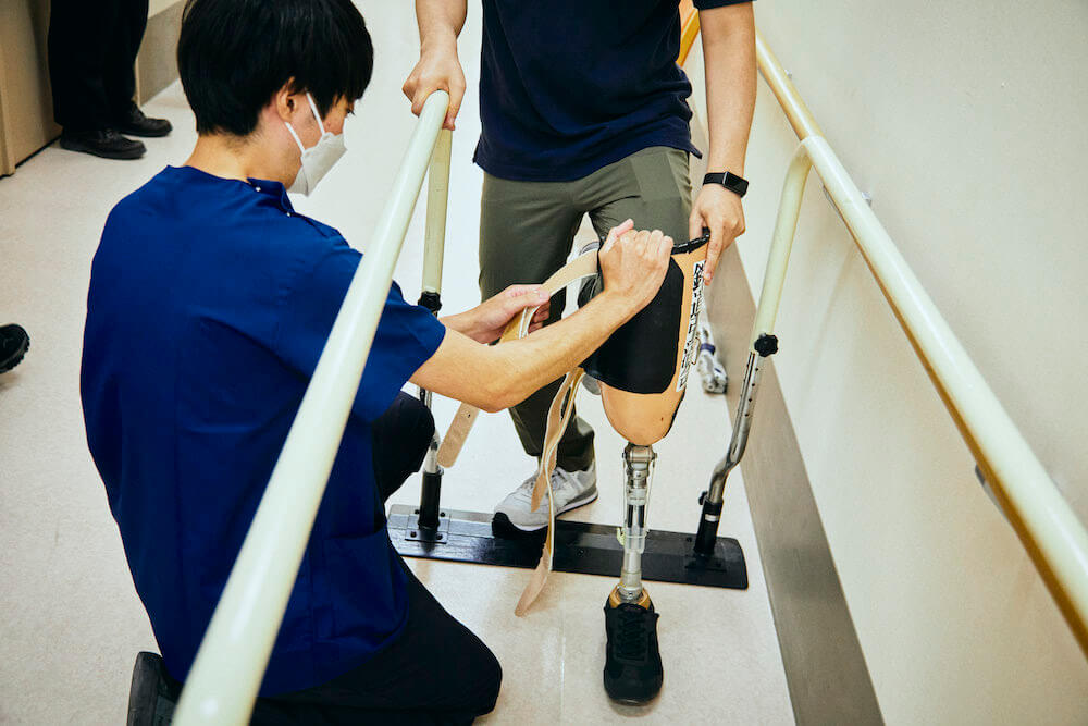 写真：理学療法士の山本さんに義足を装着してもらう日本財団ジャーナル編集部員