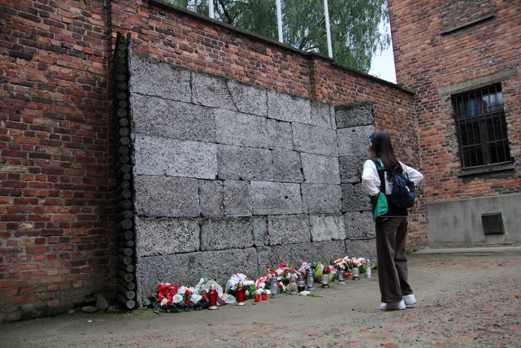 写真：アウシュビッツ＝ビルケナウ強制収容所の壁に立つ学生ボランティア