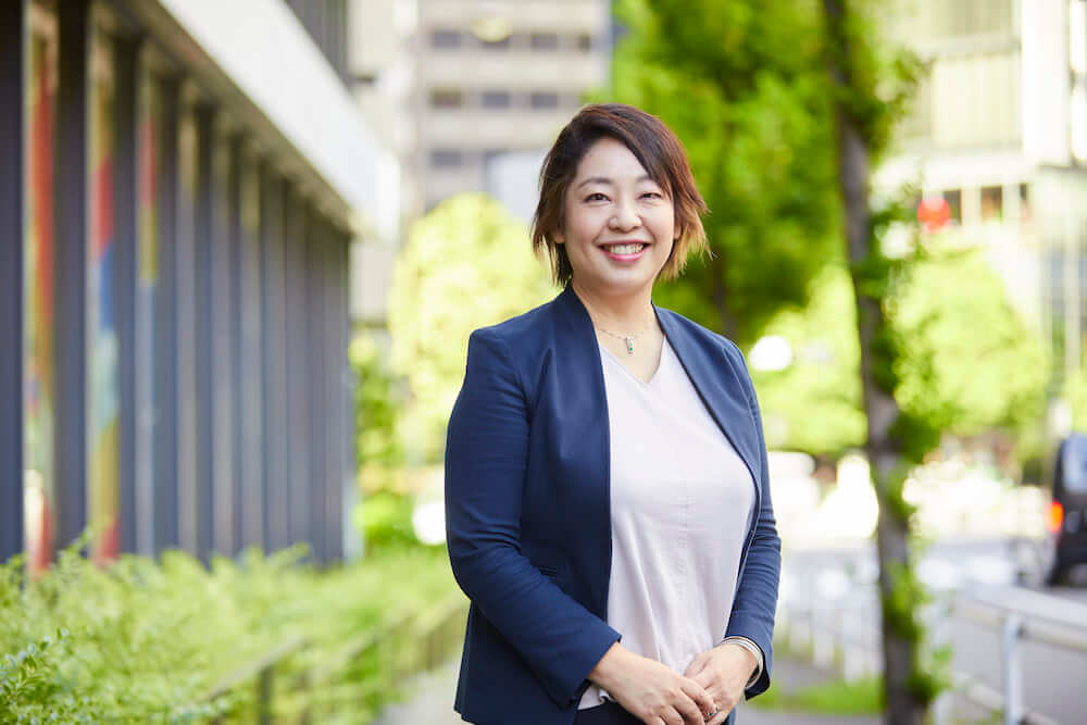 写真:街路樹を背景にして笑顔を向ける持田さん