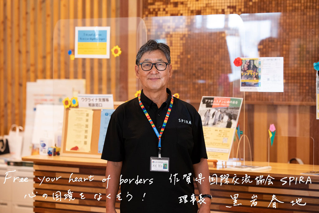 写真：佐賀県国際交流協会の黒岩春地さん。画面下側に「Free your heart borders 心の国境を無くそう！ 佐賀県国際交流協会 SPIRA 理事長 黒岩春地」の文字。