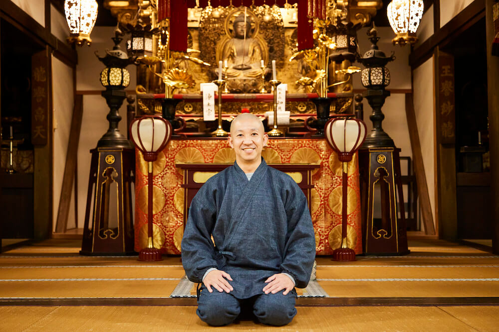 写真：安養寺の本堂にて、仏像の前で正座し優しい笑顔を向ける松島さん