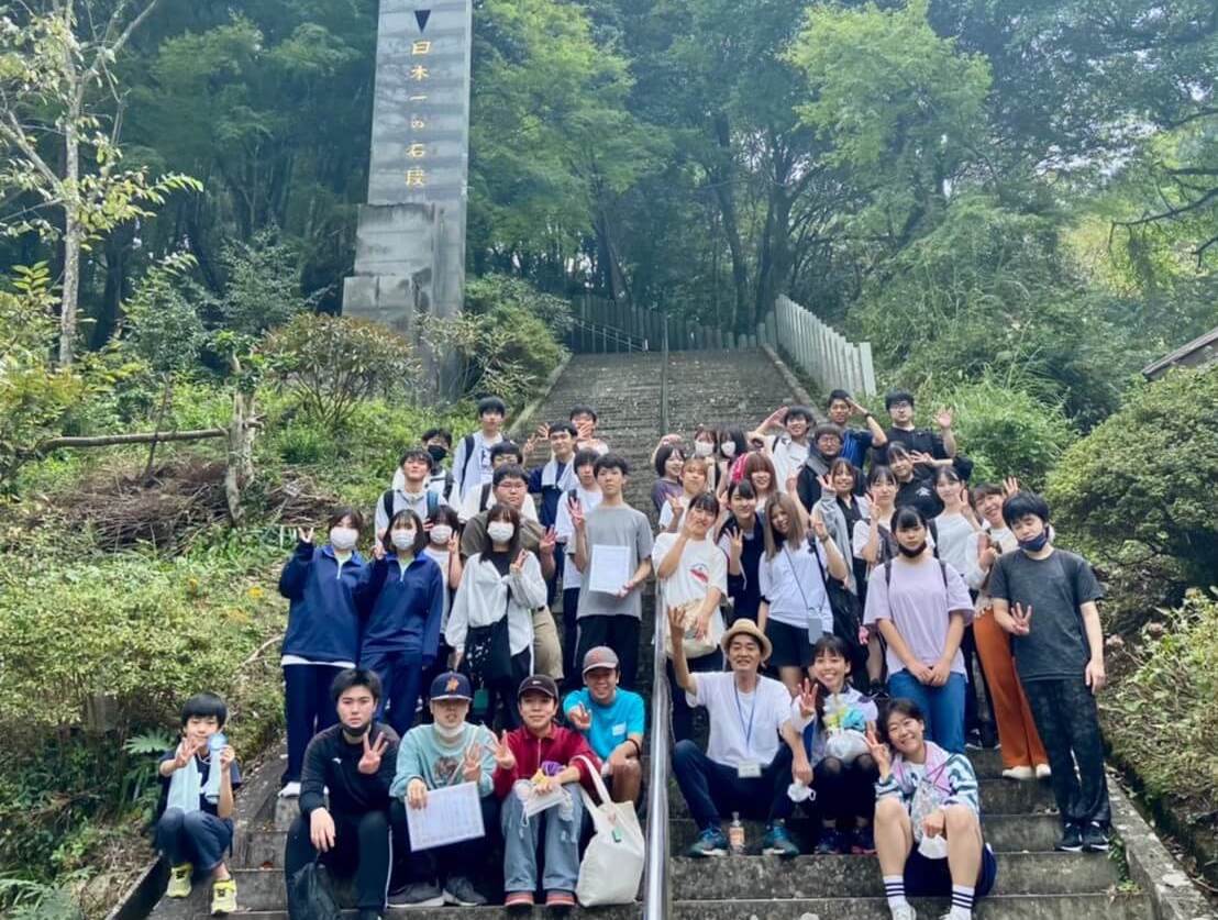 写真：3333段の日本一の石段の上に座ったり、立ったりしてカメラにピースサインする子ども第三の居場所の子どもたちと学生スタッフ