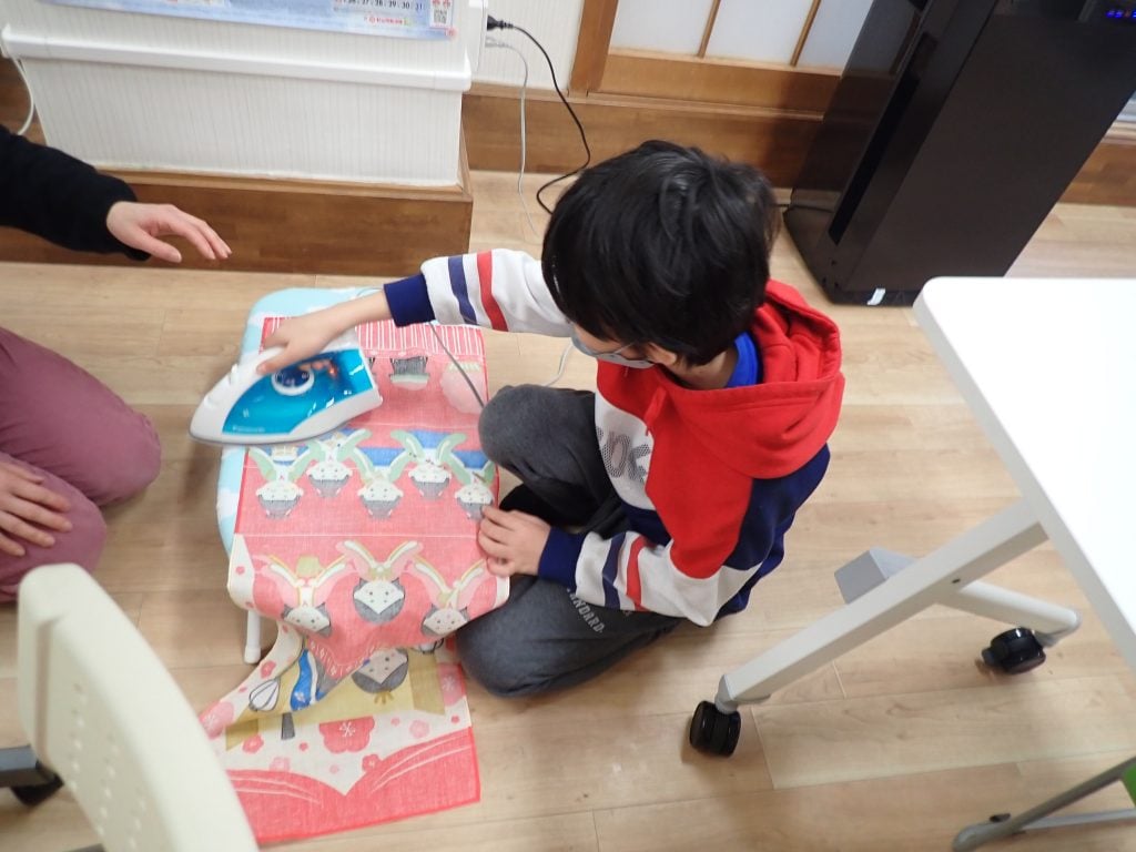 写真:スタッフからアイロン掛けを教わる子ども