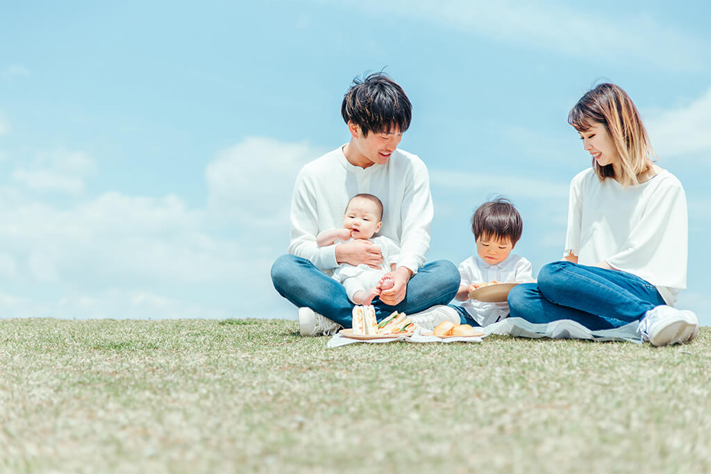 赤ちゃんと幼児の子どもがいる、家族4人がピクニックしながらご飯を食べている様子