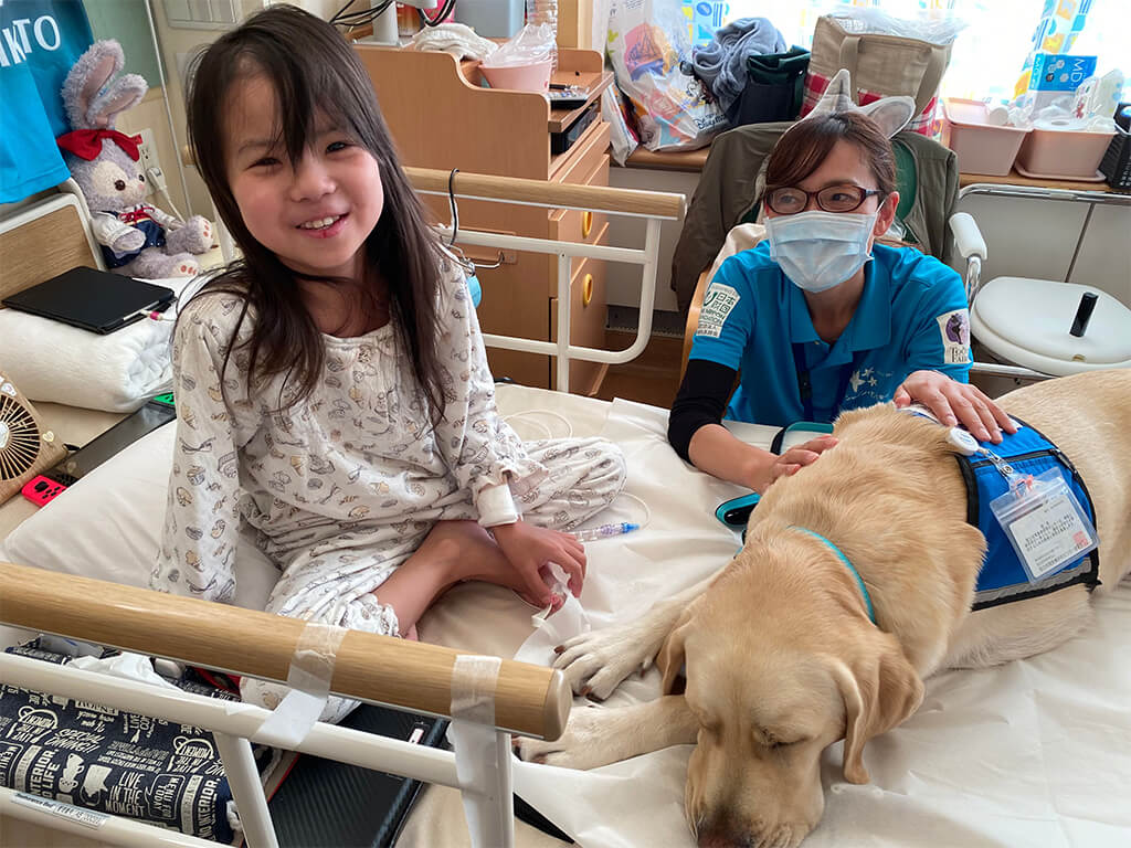 Photo of Masa lying next to a smiling child in her hospital bed