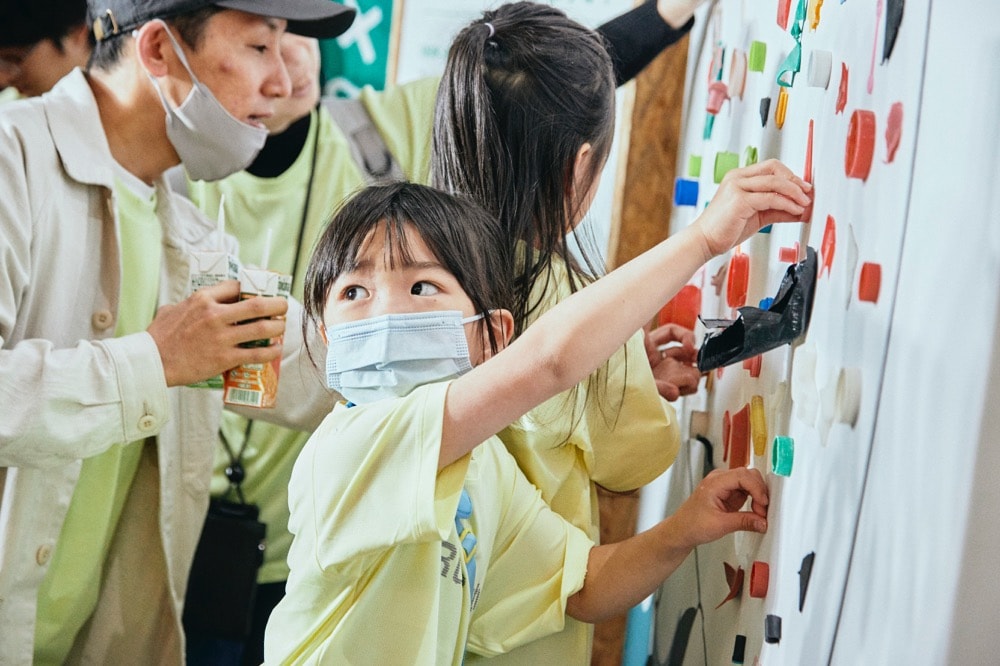 子どもが花井さんのイラストにプラスチックごみを貼り付けている様子