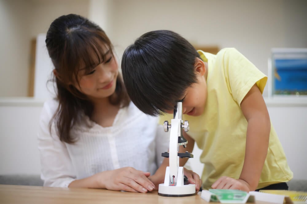 イメージ写真:顕微鏡を覗く子どもと、それを見守る母親