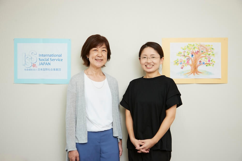 写真：ISSJのロゴとスタッフが描いた優しいイラストの横に立つ石川さんと山口さん