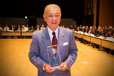 Photo of Chairman Yōhei Sasakawa of Nippon Foundation holding a commemorative shield with a smile