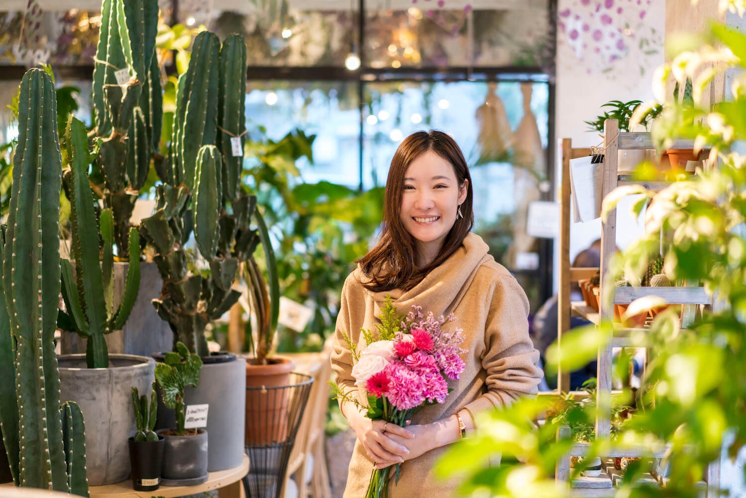 写真:お店の中で植物や花に囲まれ、手に花を持つ一般社団法人ローランズプラスの代表・福寿満希さん