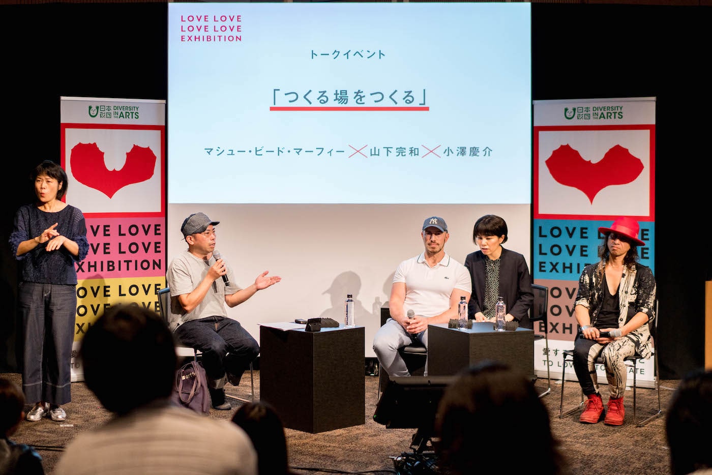 写真:トークイベントで司会をするキュレーターの小澤慶介さん(写真左から2番目)と登壇者のマシュー・ビード・マーフィーさん(写真右から3番目)、山下完和さん(写真右端)。左端には手話通訳者、マシューさんの右隣には通訳者もいる。