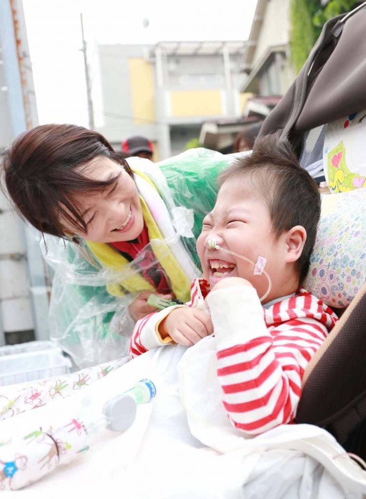 写真:笑顔の難病の子どもと、笑顔でケアをするボランティアの女性